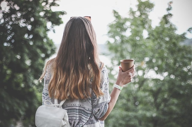 Millennial travelling in the forest holding a coffee and backpack