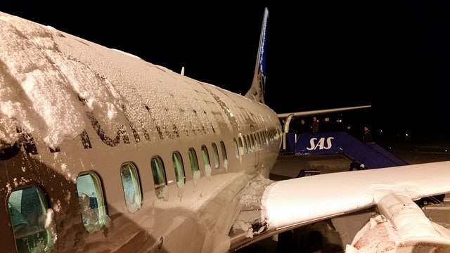Airplane covered in snow on runway experiencing delays due to winter weather